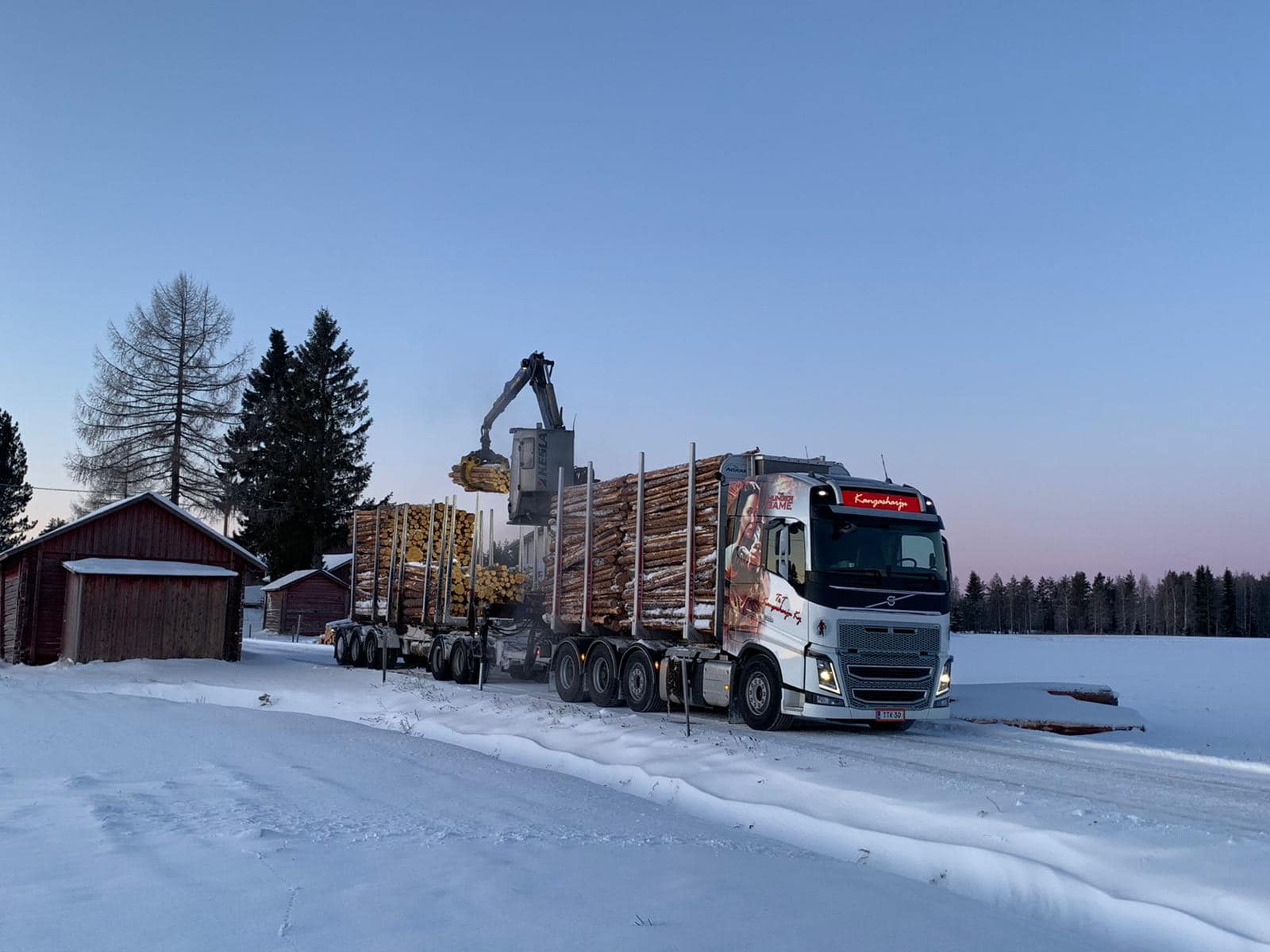 Lastataan tukkeja puunkuljetusautoon lumisessa maisemassa_Kärsämäki: T&T Kangasharju ajaa.